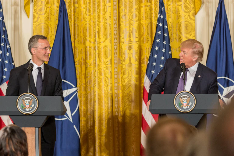 Donald Trump (right) and Jens Stolenberg standing in front of flags.