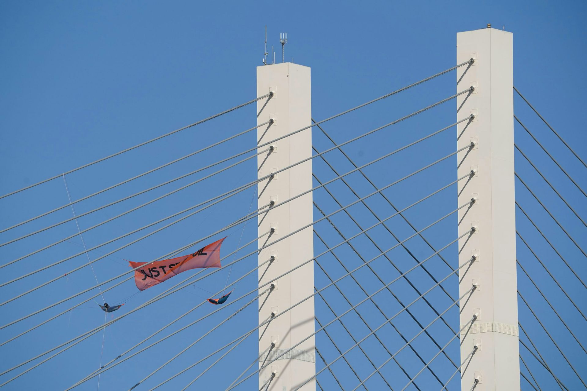 Two people in harnesses hang suspended from a bridge with a Just Stop Oil banner.