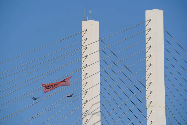 Two people in harnesses hang suspended from a bridge with a Just Stop Oil banner.