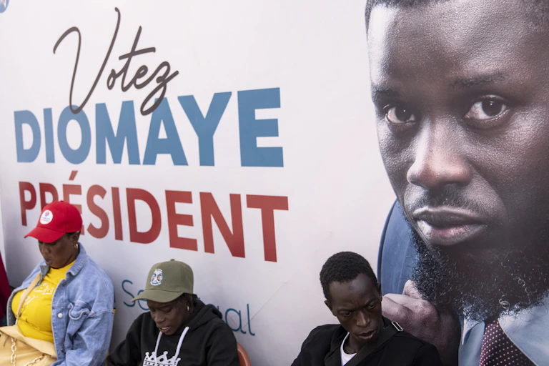 Trois personnes se tiennent devant l'affiche politique du candidat Bassirou Diomaye Faye