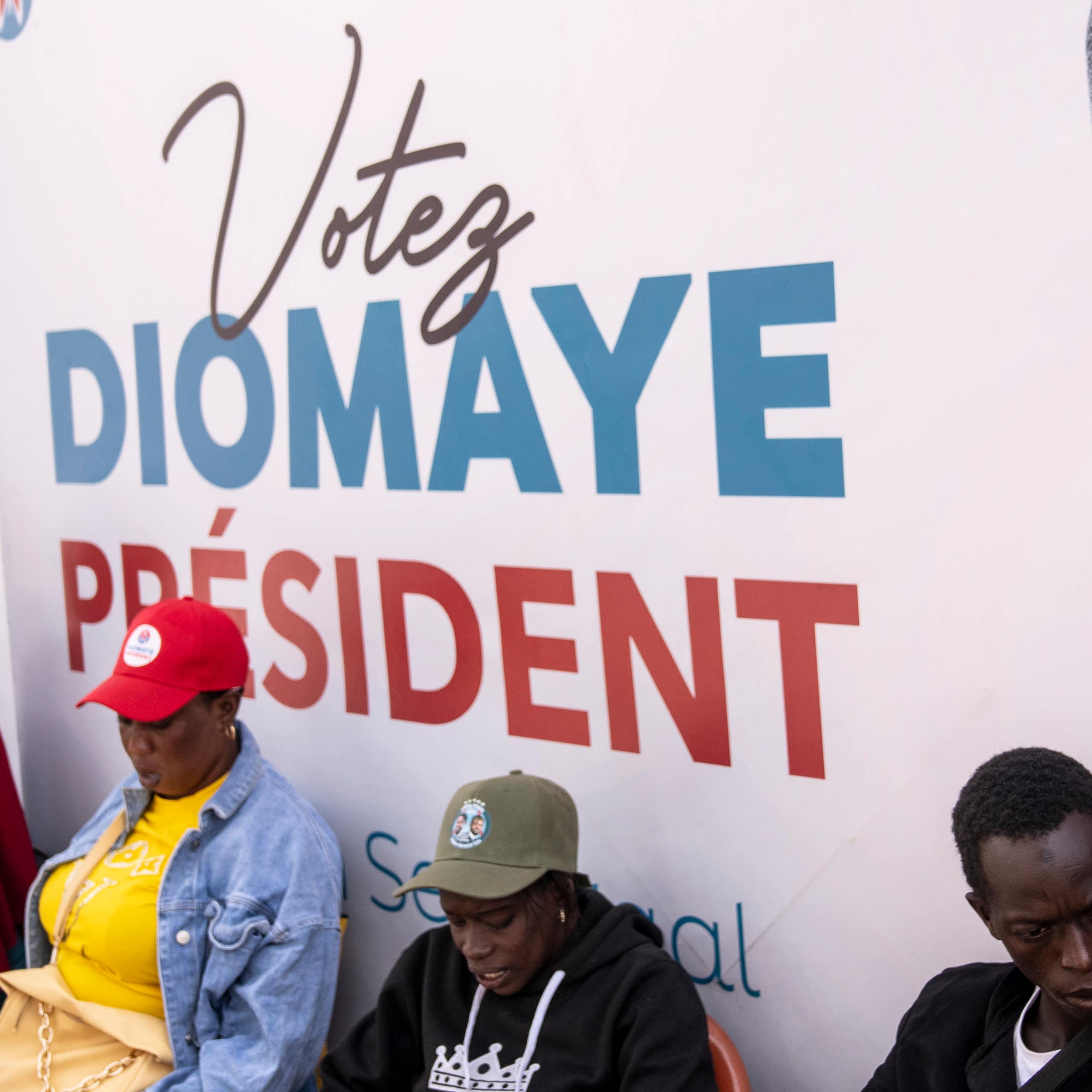 Trois personnes se tiennent devant l'affiche politique du candidat Bassirou Diomaye Faye