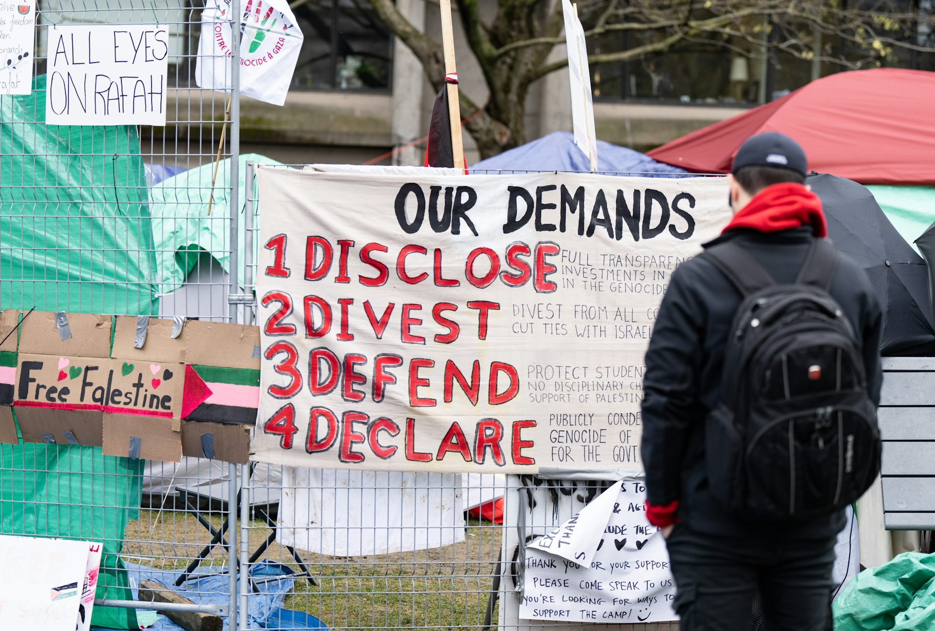 A person reads a sign that says our demands: disclose, divest, defund, declare.