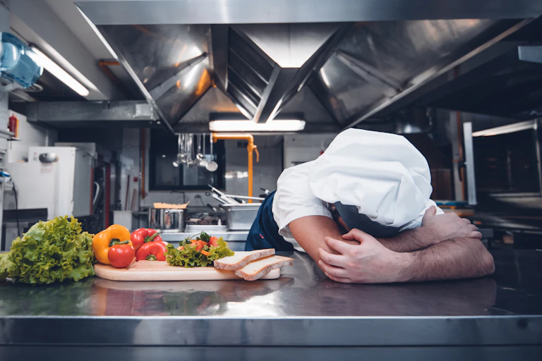 Chef with head on table in professional kitchen