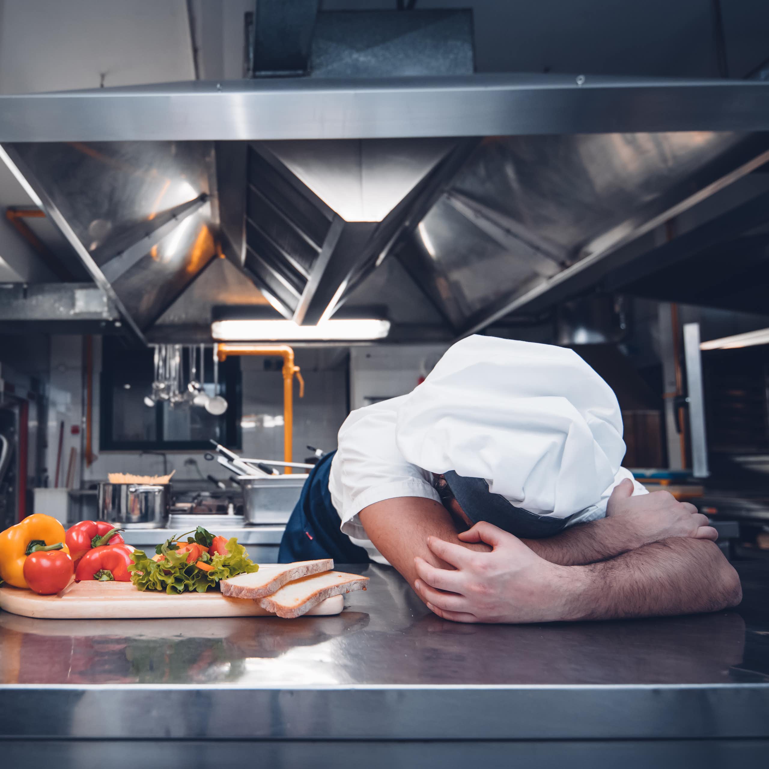 Chef with head on table in professional kitchen
