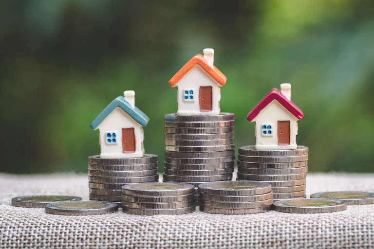 Close up of three stacks of coins with mini house figurines on top