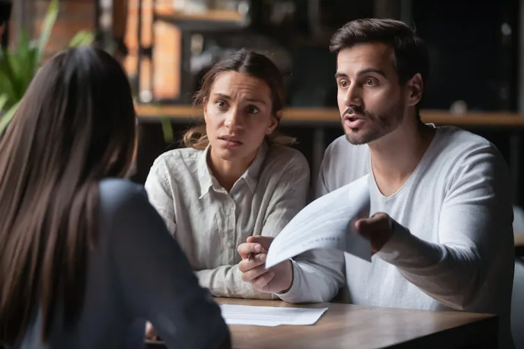 A frustrated worried young couple sitting at a desk across from a banker