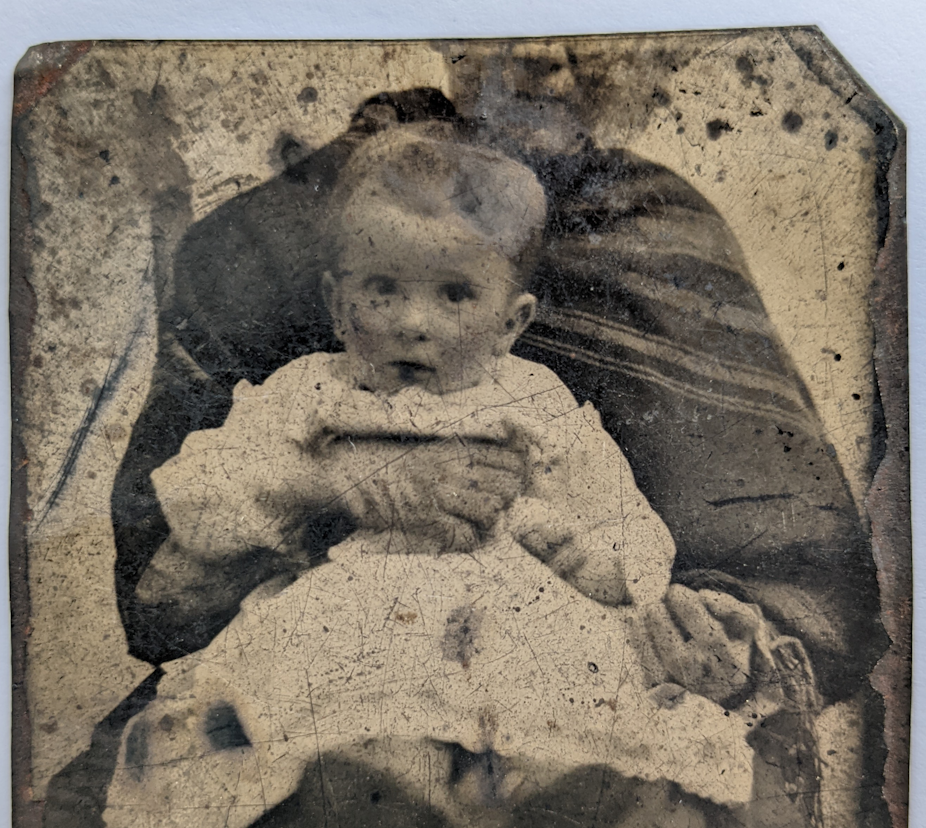 Sepia photograph of toddler held in lap of adult with half of head cut off