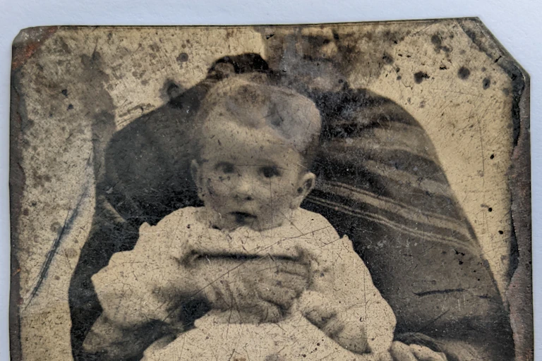 Sepia photograph of toddler held in lap of adult with half of head cut off