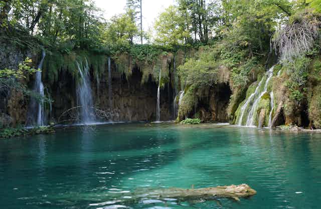 A turquoise lake with streams of water falling into it.