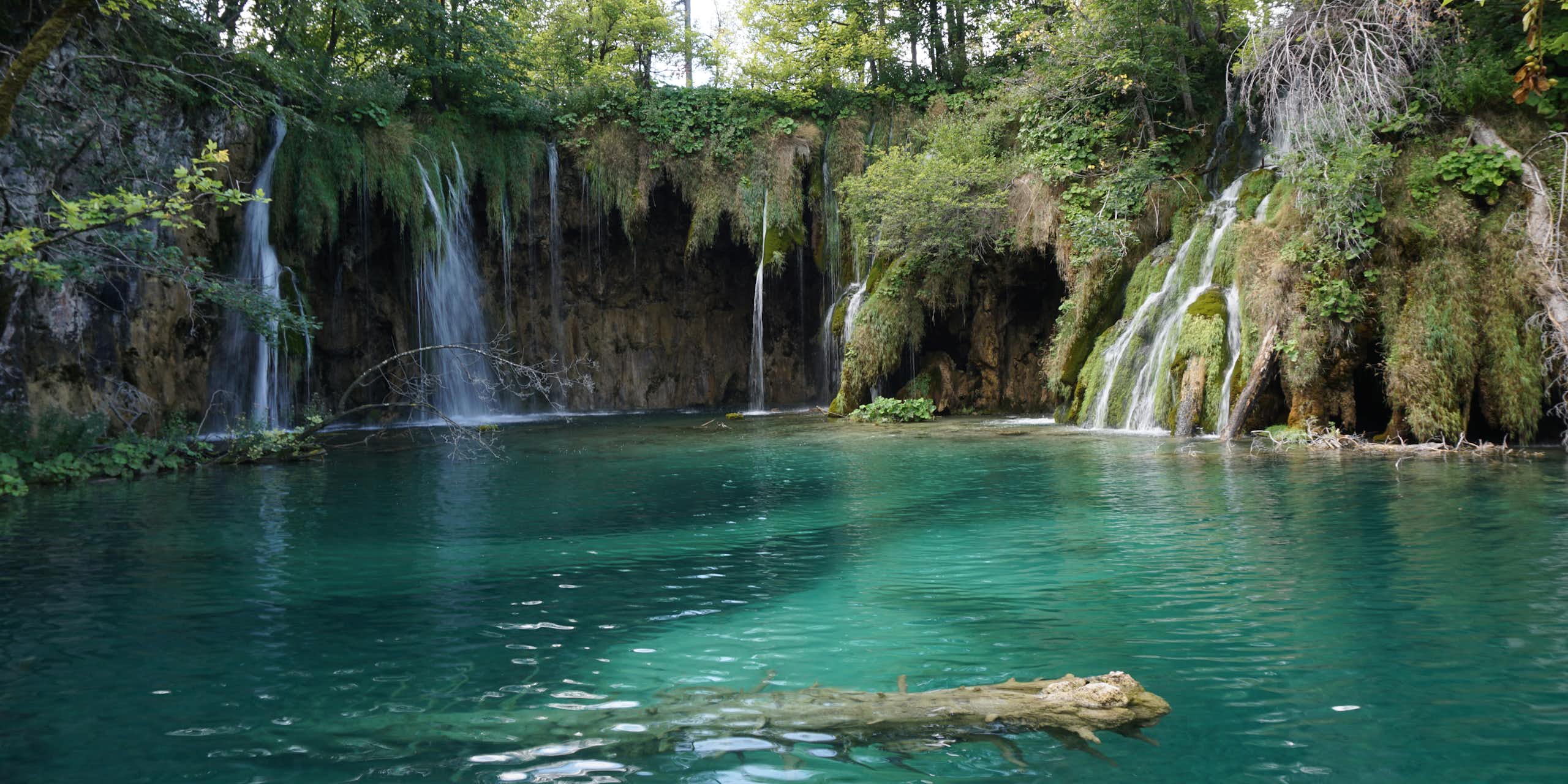 A turquoise lake with streams of water falling into it.