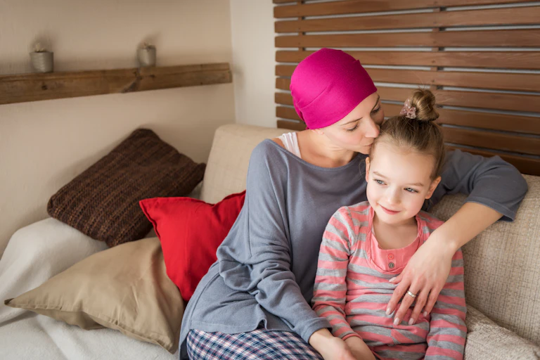 Mother wearing headscarf cuddling daughter on sofa