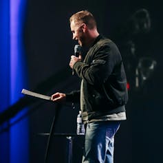 a man in a leather jacket standing on a stage in a church holding a microphone