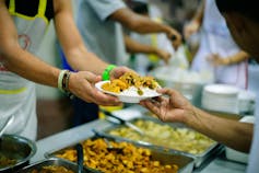 Volunteer at soup kitchen hands someone a plate of food.