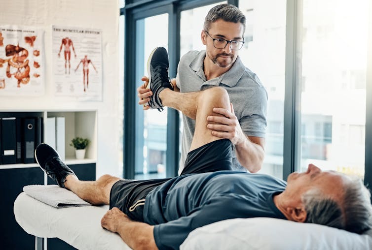 A physio flexes a patient's knee.