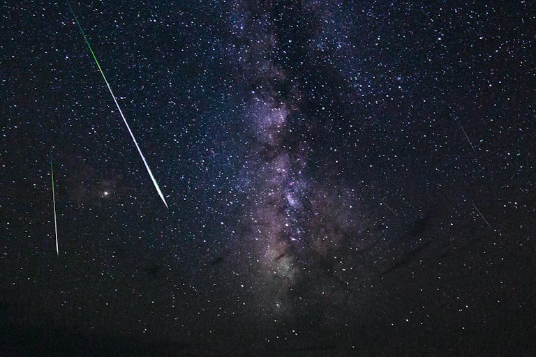 Two shooting stars in the night sky above dark mountains.