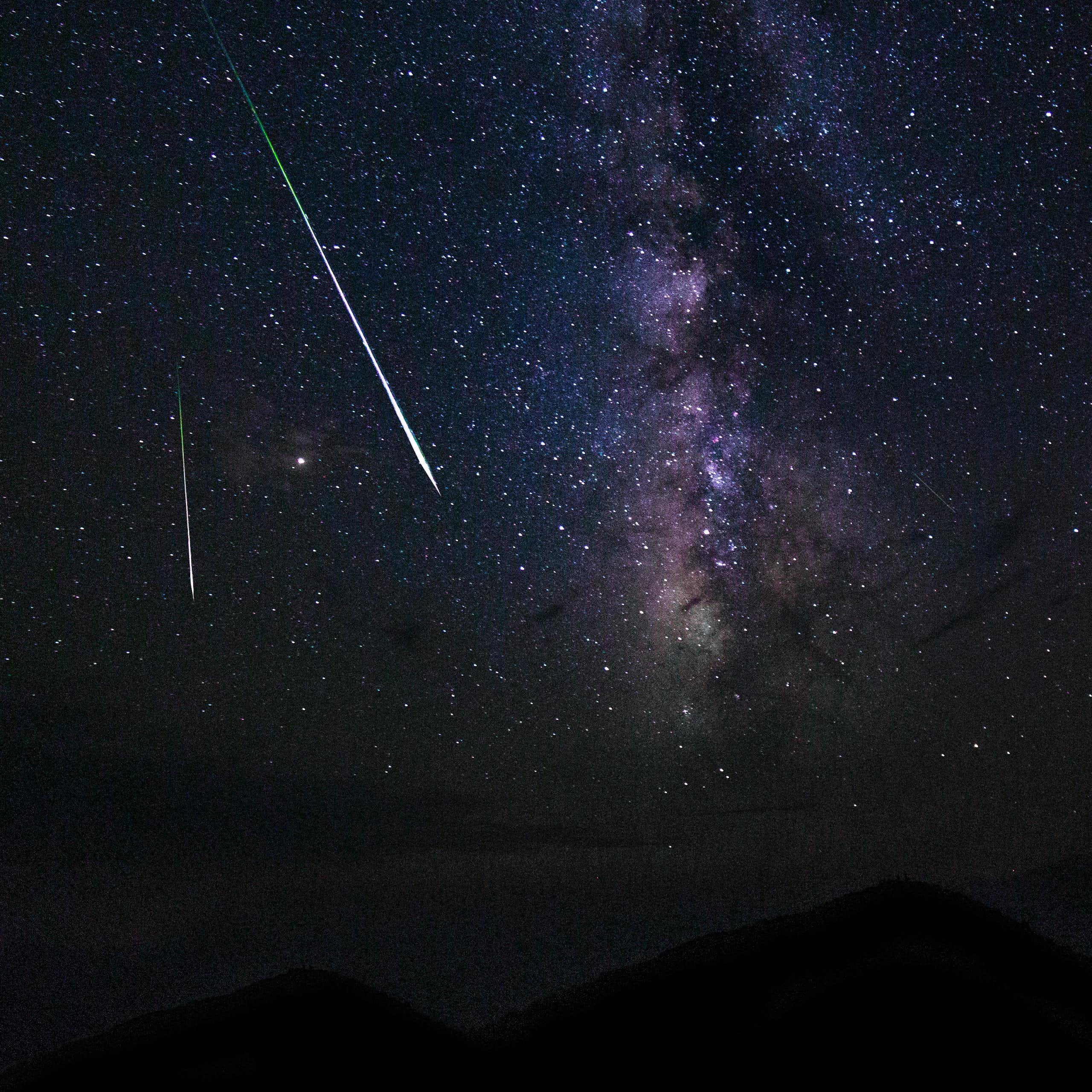 Two shooting stars in the night sky above dark mountains.
