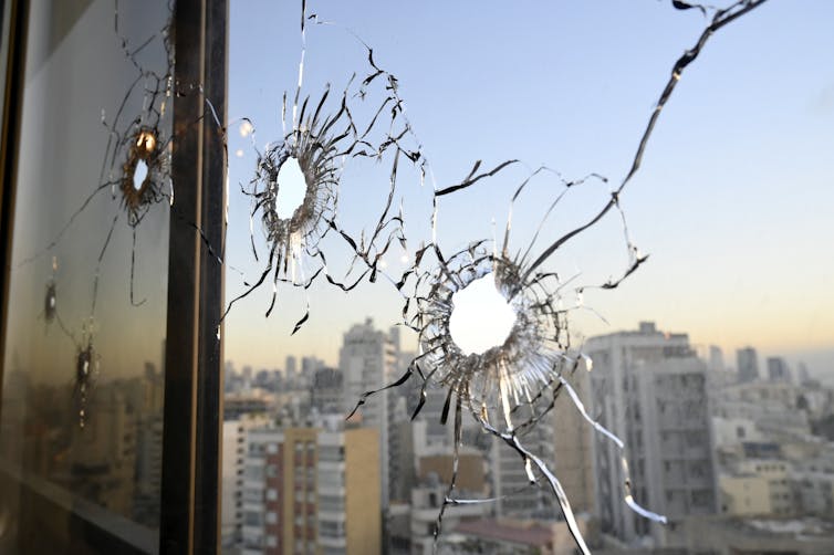 A photo taken at dusk of a window damaged by three bullet holes.