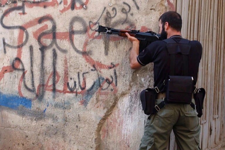 A gunman resting his machine gun against a wall.