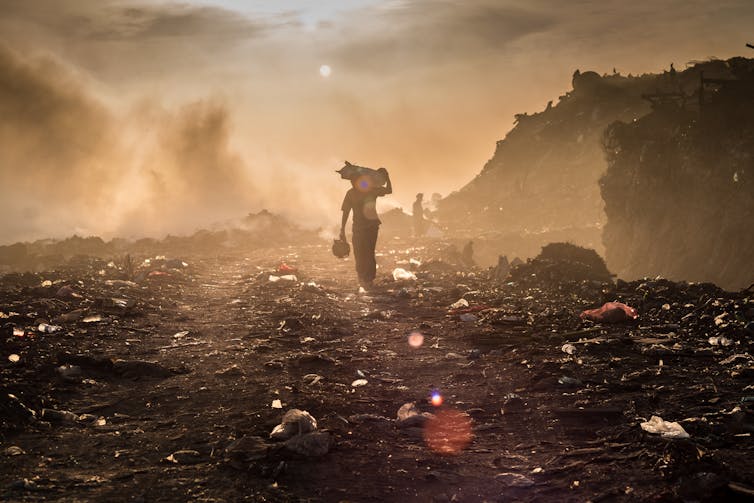 A waste picker walks across a dumpsite with burning rubbish.