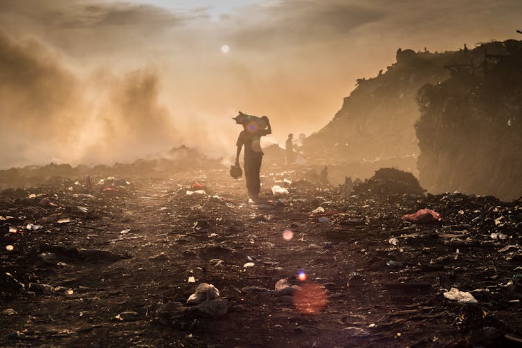 A waste picker walks across a dumpsite with burning rubbish.