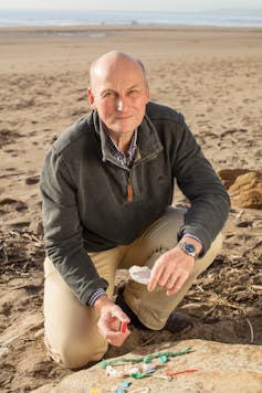 beach with man looking at camera, fragments of plastics on rock in foreground