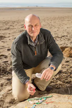 beach with man looking at camera, fragments of plastics on rock in foreground