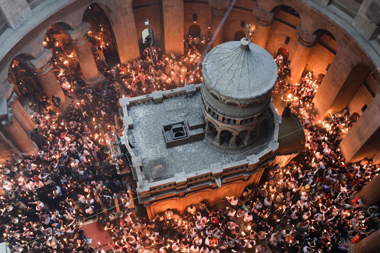 An aerial shot of a crowd of people in a church holding lit candles.