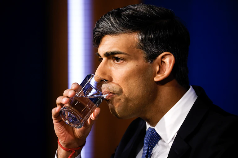 Rishi Sunak drinking a glass of water, looking tense.