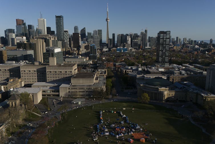 An encampment seen from an aerial view in the context of the Toronto skyline showing skycrapers and the CN tower.