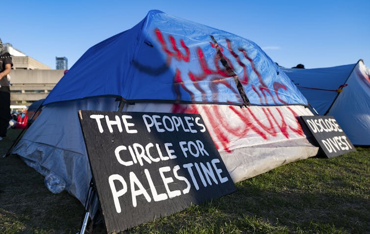A protester attaches a banner to a tent at an encampment set up on the University of Toronto campus on May 2, 2024.