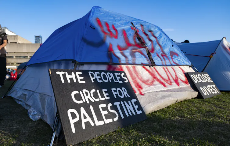 A protester attaches a banner to a tent at an encampment set up on the University of Toronto campus on May 2, 2024.
