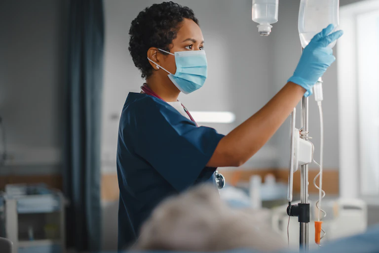 A nurse in a face mask and gloves administering an IV