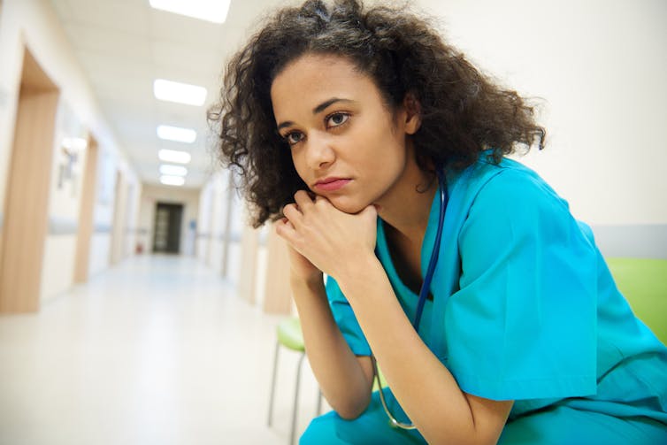 A nurse in scrubs sitting with her chin in her hands
