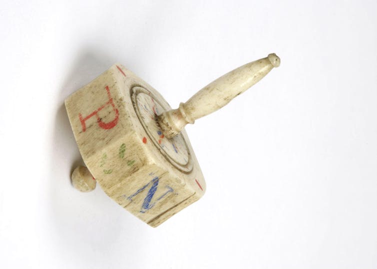 An old wooden game spinner akin to a dreidel with faded, colored markings.