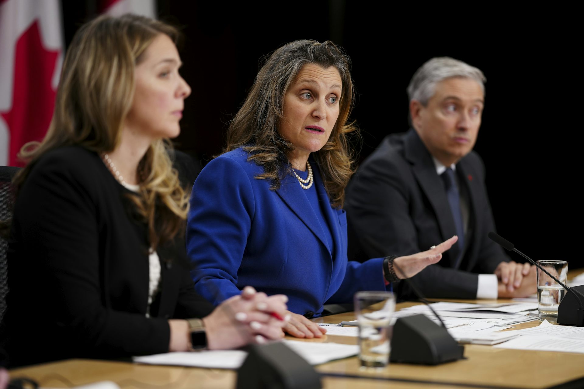 Two women and a man sit behind a table and speak to an audience off-screen