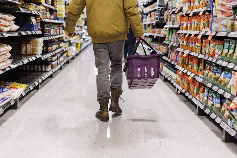 A person seen from the shoulders-down walking away from the camera down a grocery store aisle