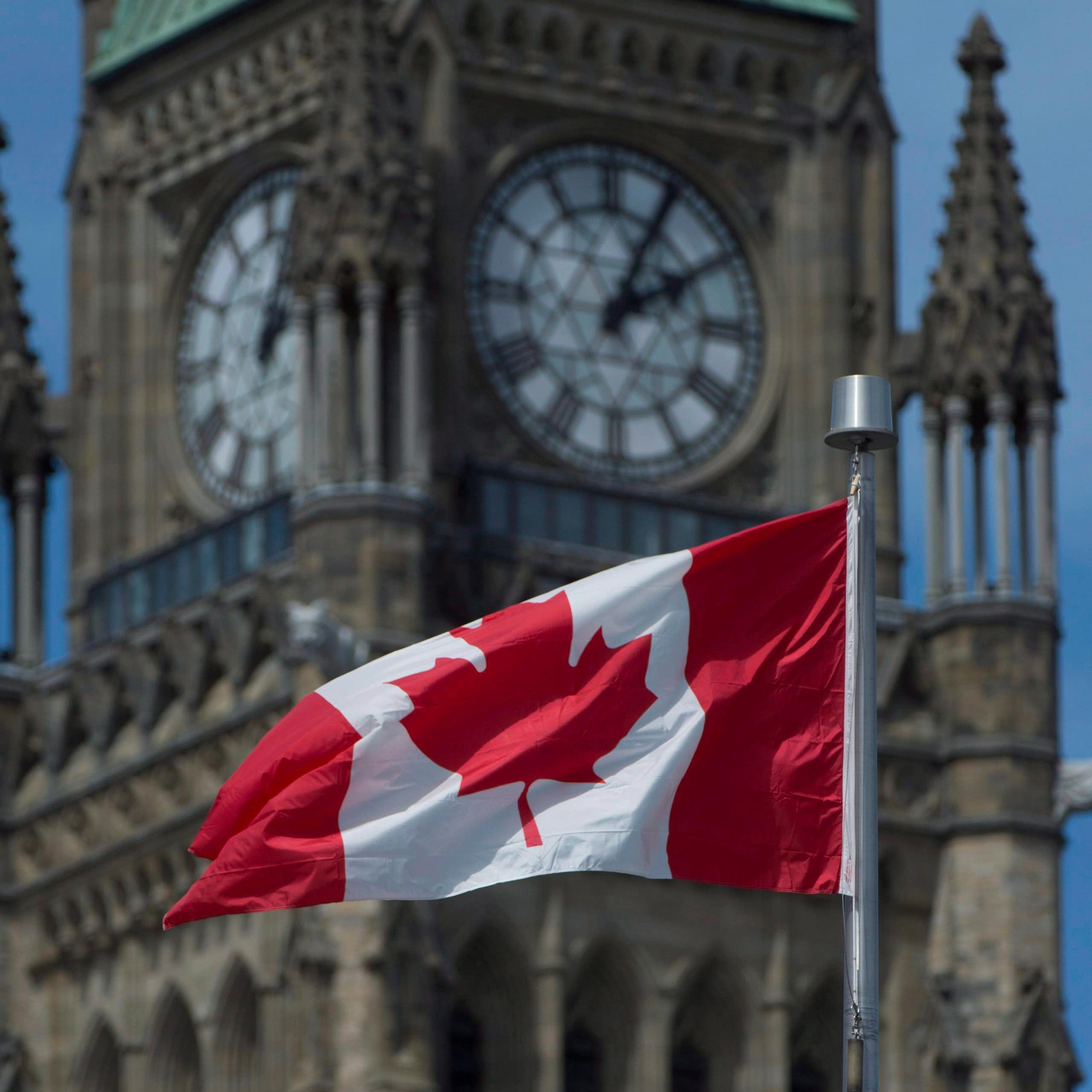 A Canadian flag flying in front of an old-fashioned clock tower