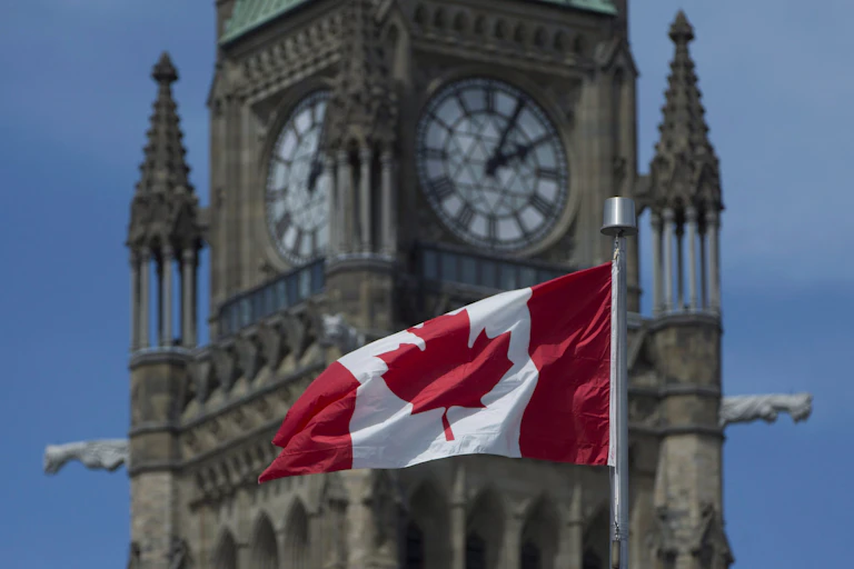 A Canadian flag flying in front of an old-fashioned clock tower