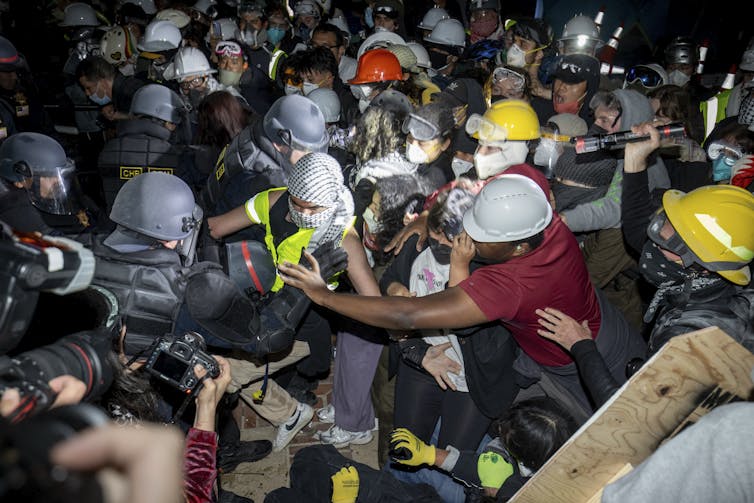 Police and protesters tussle, with people in both groups wearing helmets.