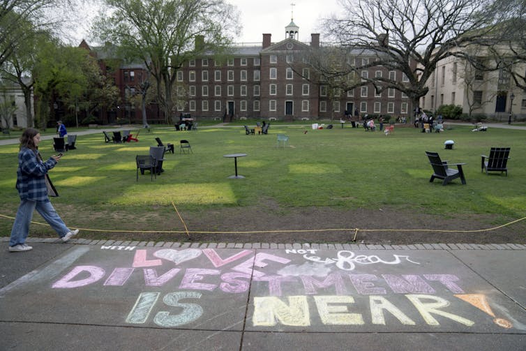 A message in chalk decorates a sidewalk on a college campus, including the words 'Divestment is near.'