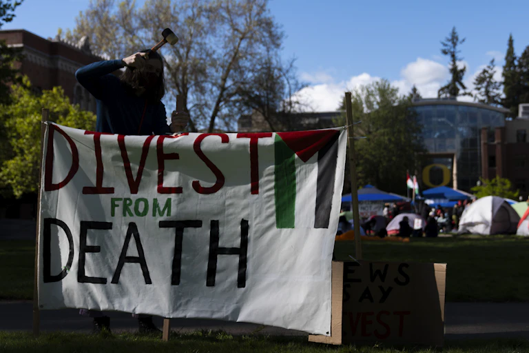 A student at the University of Oregon sets up a sign that reads 'Divest from death' at a campus encampment.