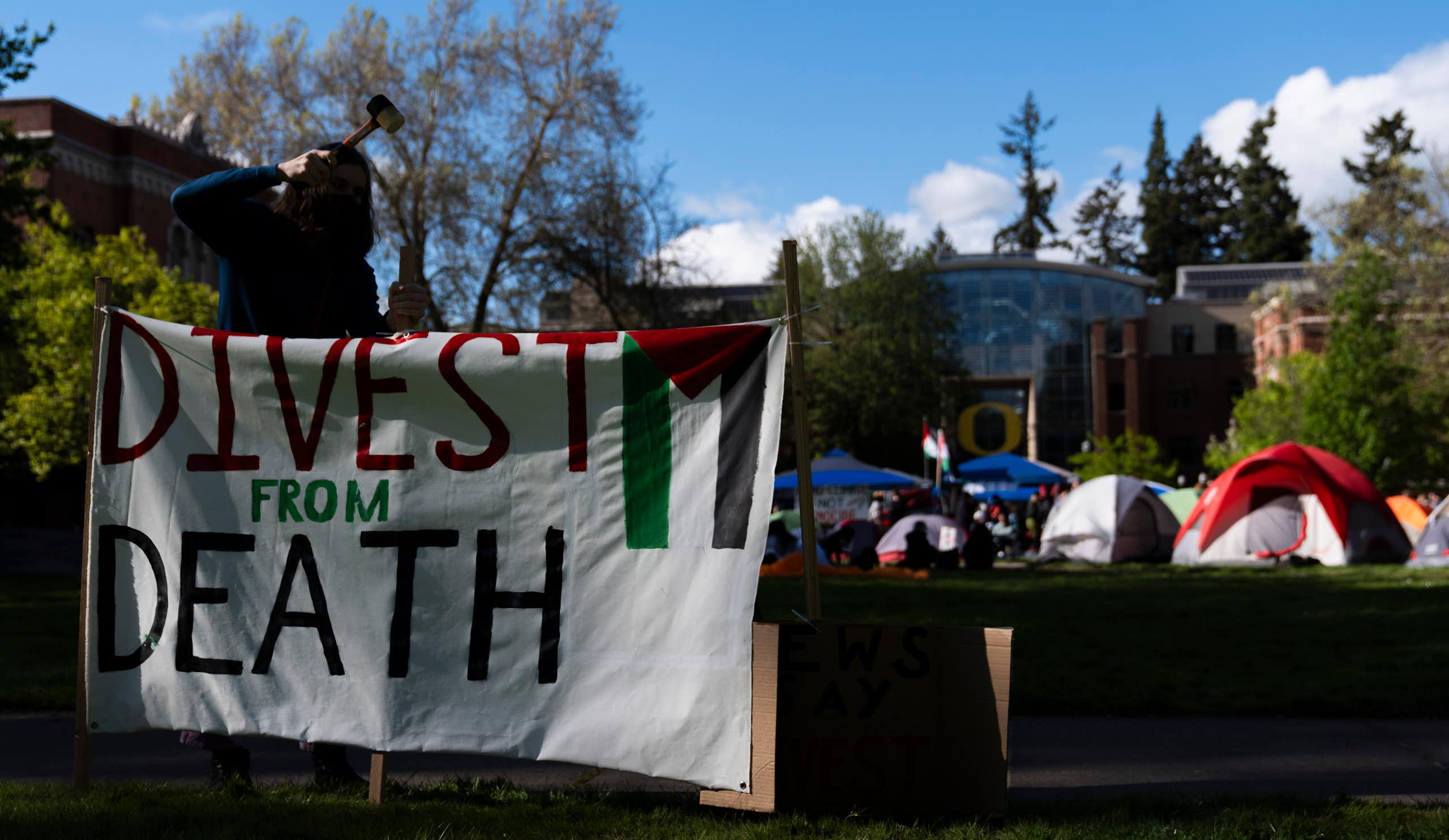 A student at the University of Oregon sets up a sign that reads 'Divest from death' at a campus encampment.