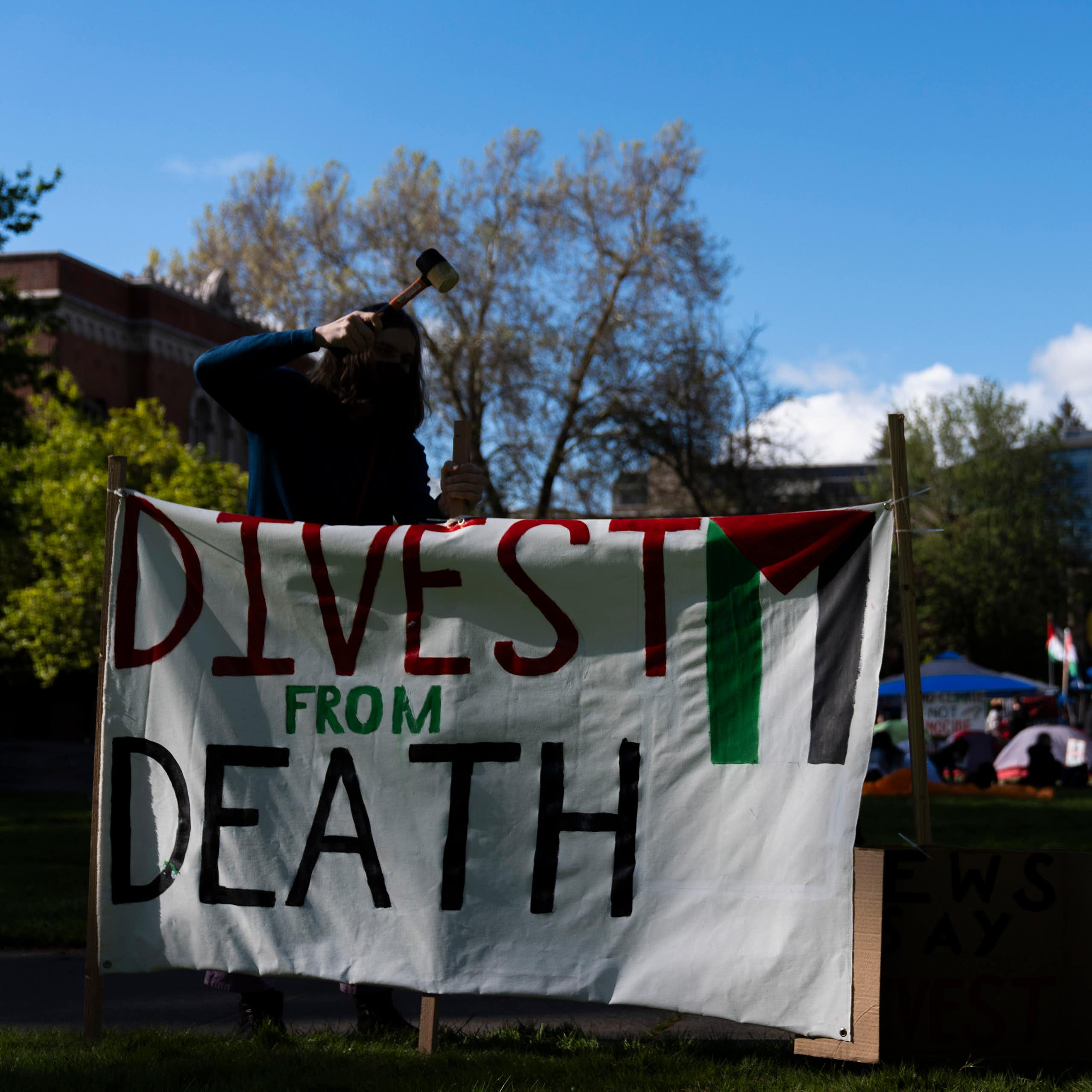 A student at the University of Oregon sets up a sign that reads 'Divest from death' at a campus encampment.