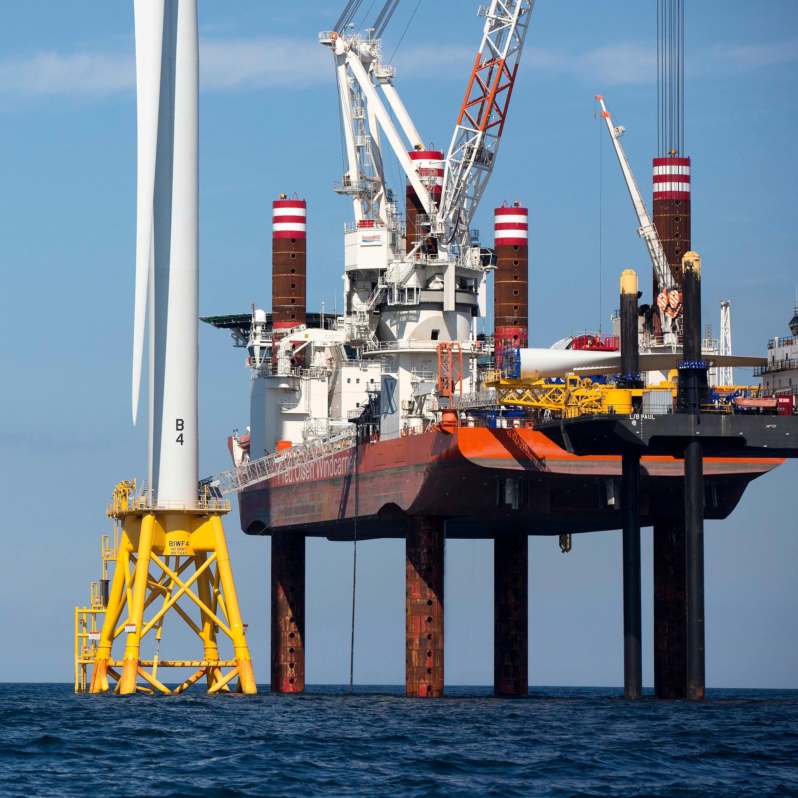 A large ship on stilts that stabilize it uses cranes to build giant offshore wind turbines and their posts.