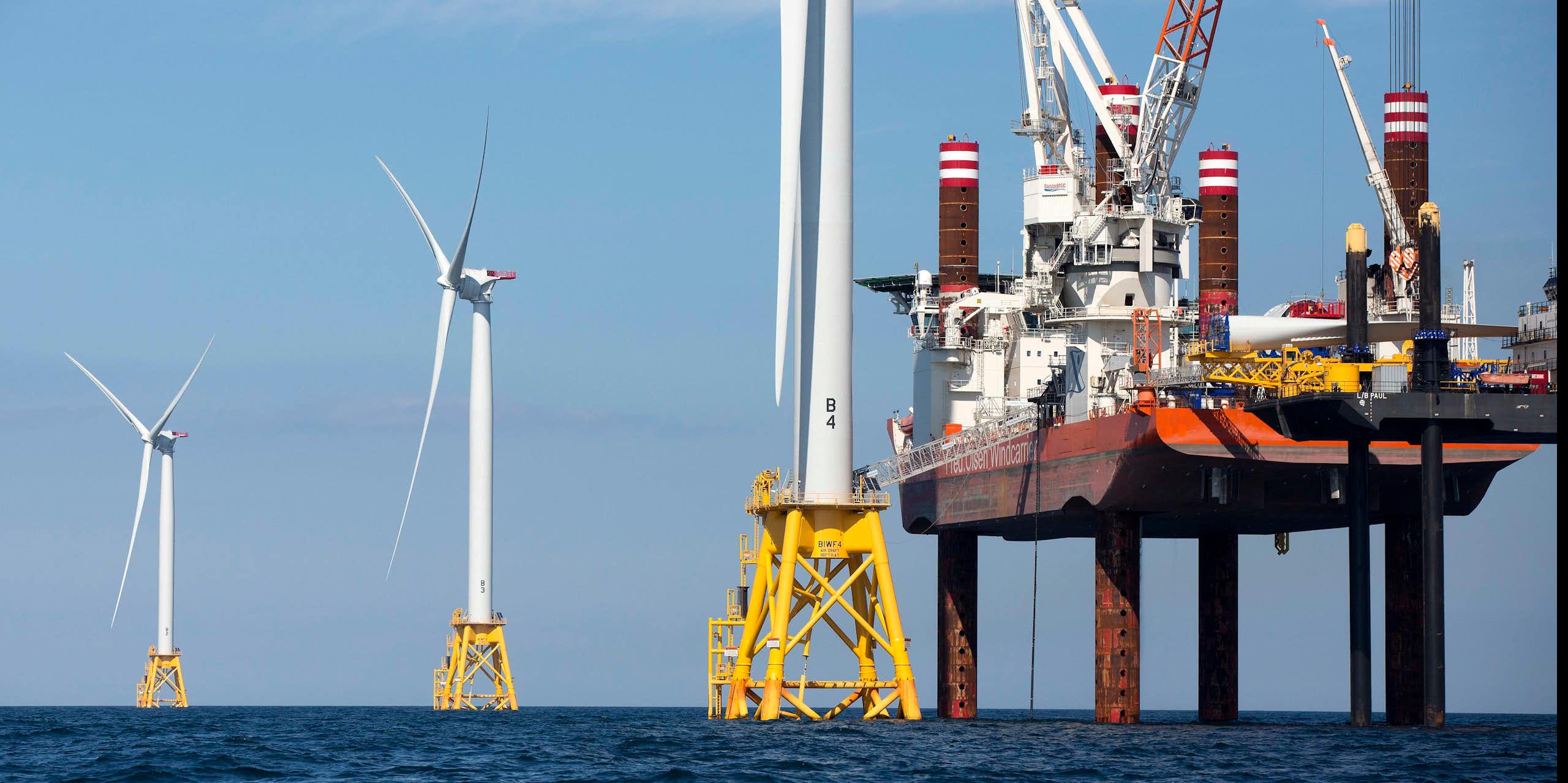 A large ship on stilts that stabilize it uses cranes to build giant offshore wind turbines and their posts.