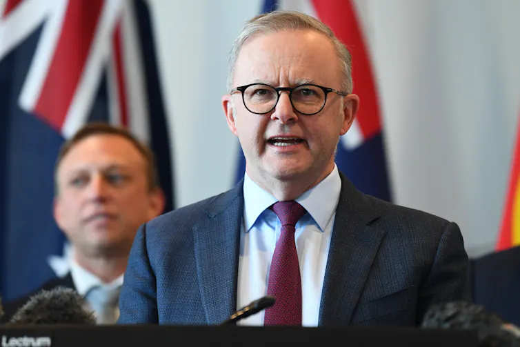 A man in glasses and a suit stands behind a lectern and gives a speech