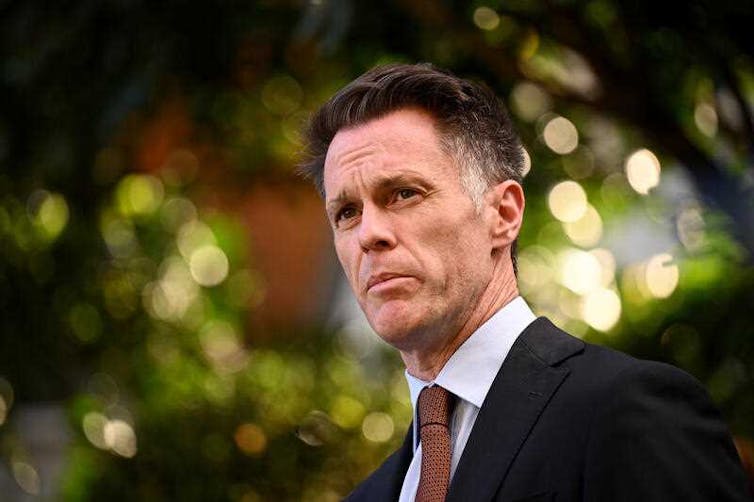 A man in a suit and tie looks past the camera against an out of focus green background