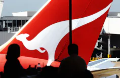 Waiting passengers seen silhouetted against tail of a Qantas plane