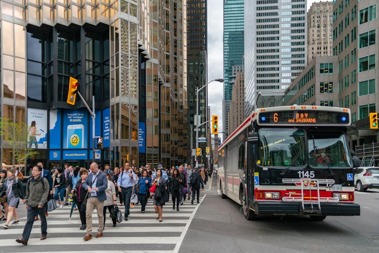 a stream of people in business attire crossing a street next to a Toronto transit bus