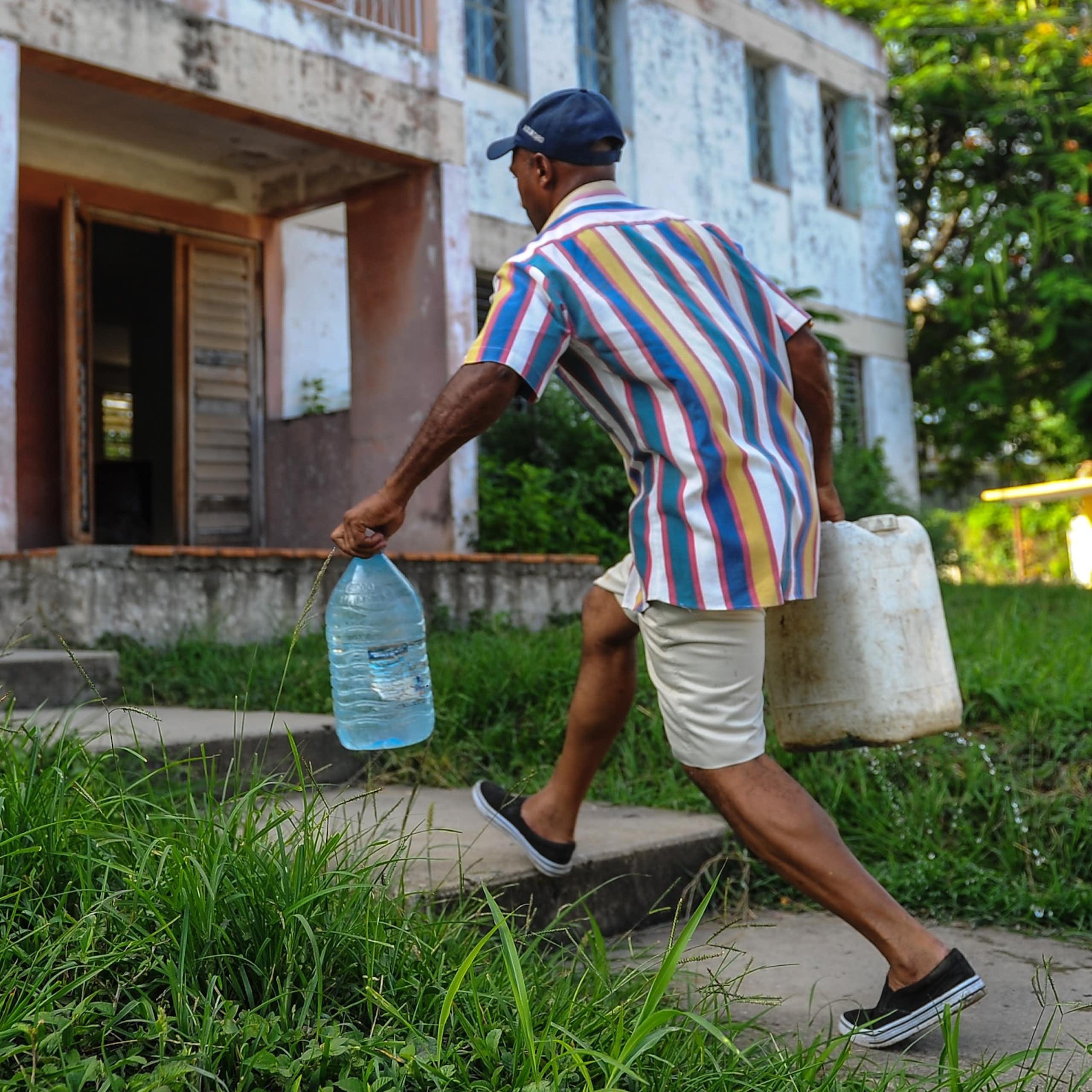 A man carries two large jugs of water to an apartment building.